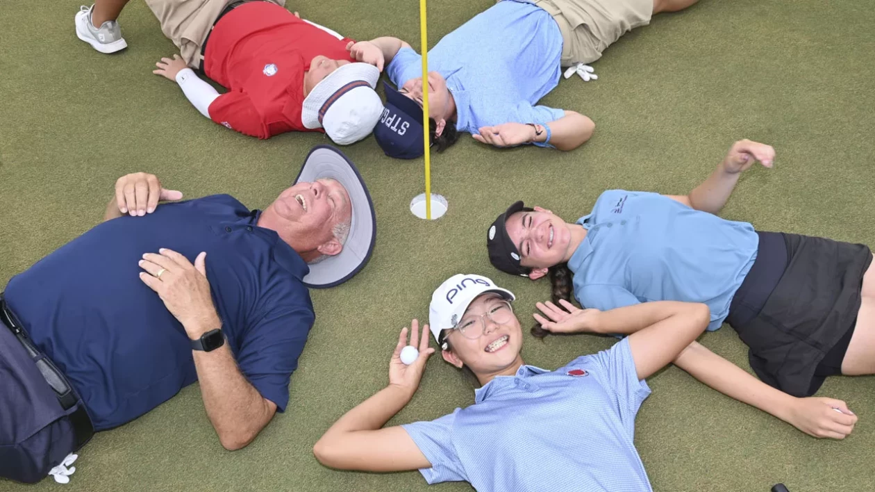 group of smiling people lying down on the green next to the pin